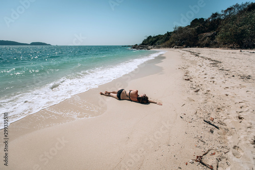 Beautiful young woman in bikini llying at the sunny sandy beach of the Andaman sea