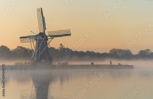 Scooter by a traditional Dutch windmill during a foggy sunrise. De Helper, Groningen.