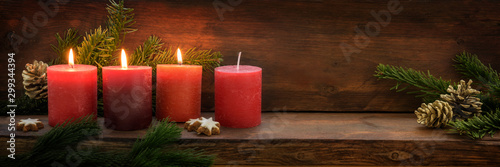 Third Advent, three of four red candles are lit with a flame, fir branches and Christmas decoration on dark rustic wood, wide panoramic format with copy space photo
