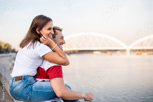 Loving couple in jeans having fun on a riverbank, doing piggyback ride
