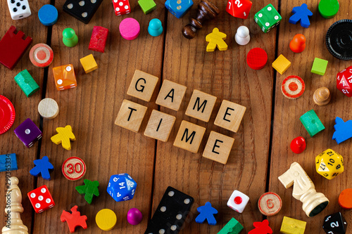 "Game Time" spelled out in wooden letter tiles. Surrounded by dice, cards, and other game pieces on a wooden background