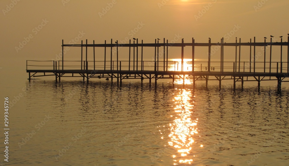 old wooden pier with silhouettes of seagulls at sunset quiet autumn evening