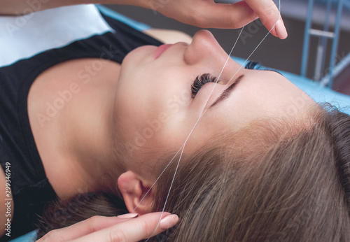 The make-up artist plucks eyebrows with a thread close-up. Professional make-up and face care in the beauty salon