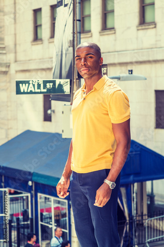 Young African American man traveling in New York City. Wearing yellow short sleeve shirt, young black college student standing on Wall Street outside office, looking forward, confident, successful. .