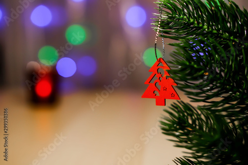 A wooden Christmas toy hangs on a lush spruce branch.The background is blurry by candlelight. Bokeh Space for text.