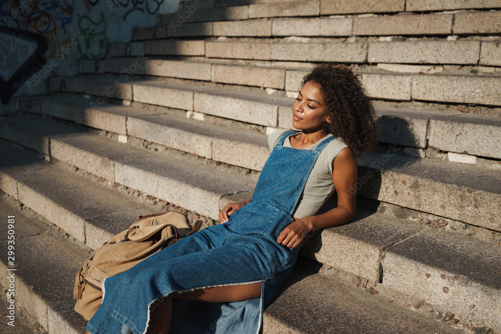 African woman sit on steps outdoors with bag by street. African woman sit on steps outdoors with bag by street.