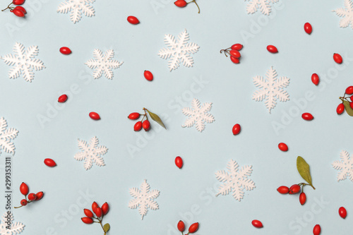 Christmas pattern made of snowflakes and red berries on pale blue background. Christmas, winter holiday, new year concept. 