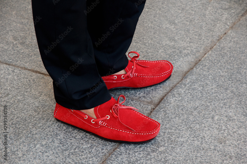 A man's feet in red suede moccasins with leather lace and black trousers outdoors