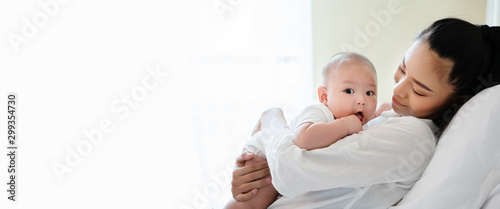 Portrait of beautiful Asian mother hugging his newborn son in the bedroom. Baby is adorable. Mom is smiling happily with the child healthy. Nursery for young children. Banner with copy space