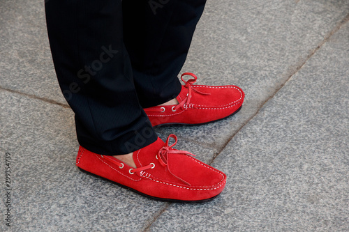 A man's feet in red suede moccasins with leather lace and black trousers outdoors © Marina
