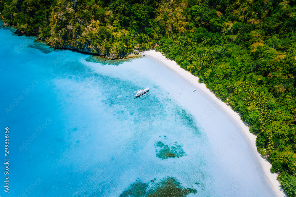 Aerial top down view of boat moored at secluded white sand beach with coconut palm trees and surreal turquoise blue shallow lagoon around. Travel exotic paradise concept