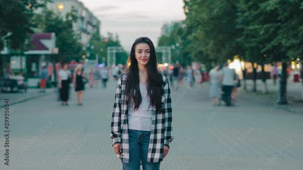 Time lapse of attractive young woman smiling in city street in crowd of people looking at camera standing alone in flow of men and women. Youth and lifestyle concept. Time lapse of attractive young woman smiling in city street in crowd of people looking at camera standing alone in flow of men and women. Youth and lifestyle concept.
