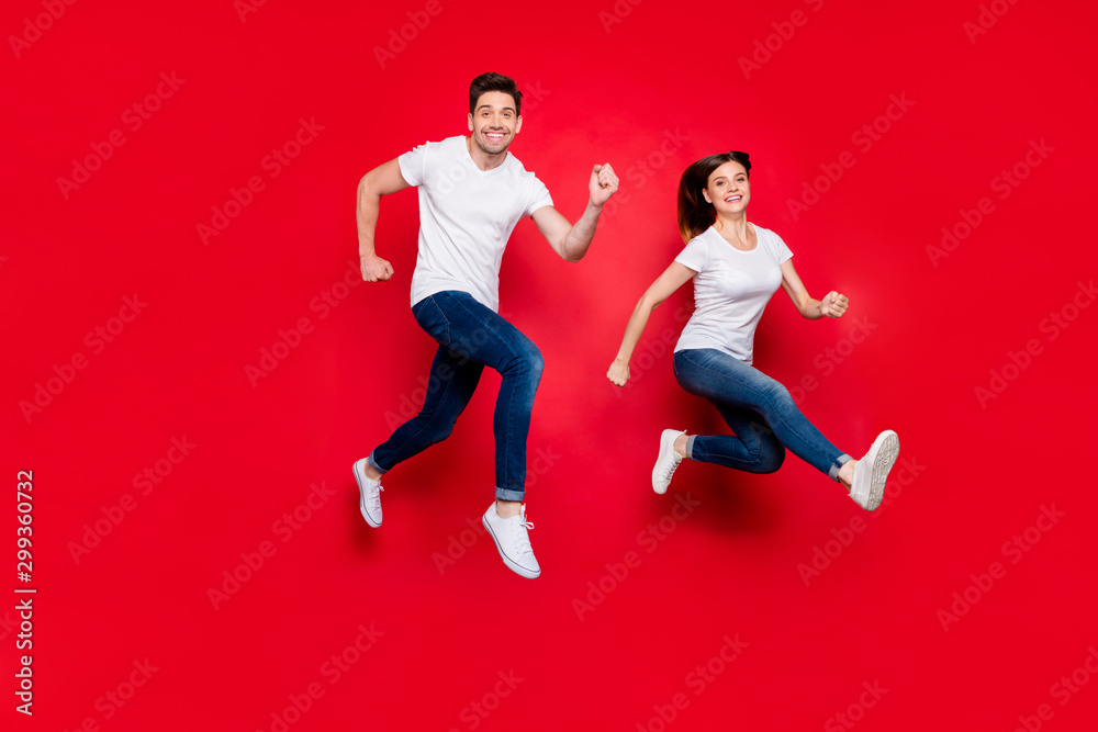 Turned full length body size photo of cheerful cute nice pretty girlfriend boyfriend spouses wearing jeans denim white t-shirt footwear smiling toothily running jumping isolated vivid color background