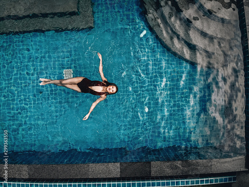 High level view of the beautiful young woman swimming in the blue pool; relaxation concept.