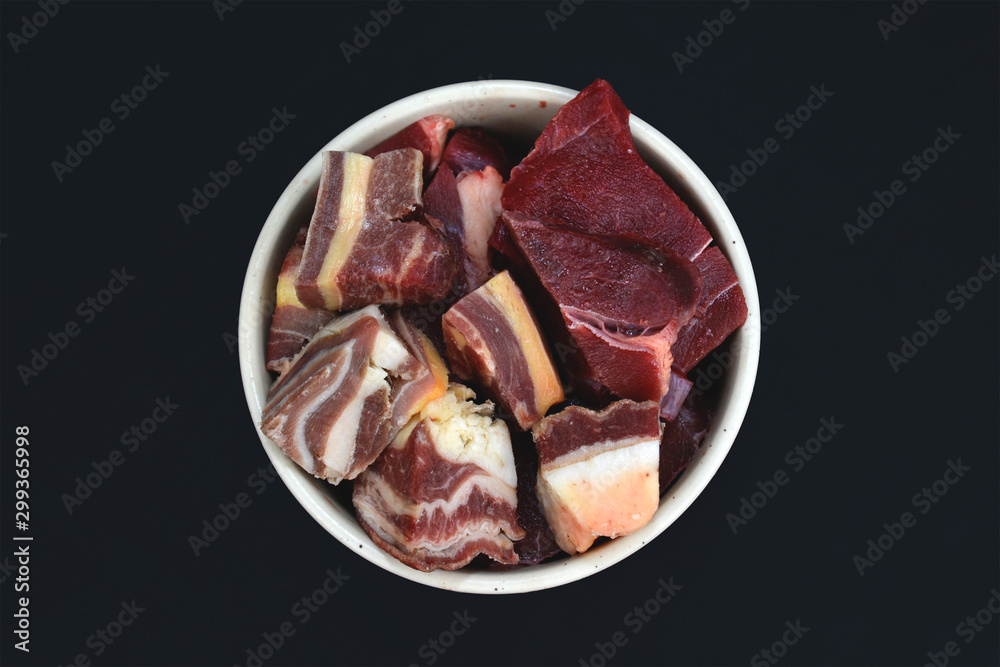 Top view of dog bowl with big red chunks of meat with fat used for dog or cat raw biologically appropriate feeding on black background