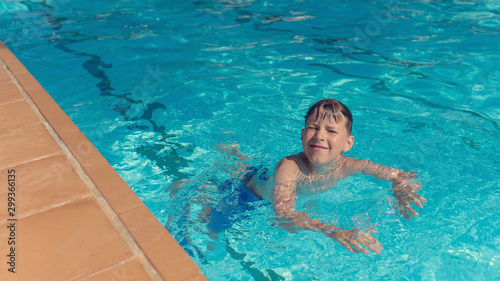 Portrait of smiling Caucasian boy spending time in pool at resort.  He is swimming in water and enjoying his summer vacations.