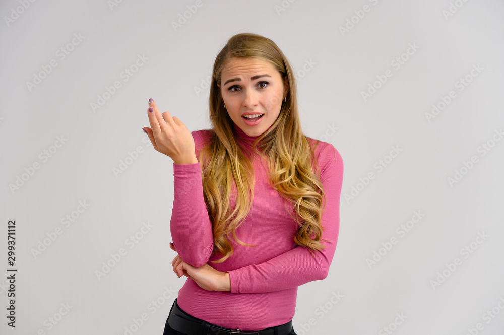 Close-up portrait of a pretty blonde girl with long curly hair standing in the studio on a white background with emotions in different poses in a pink sweater. Beauty, Model, Cosmetics Close-up portrait of a pretty blonde girl with long curly hair standing in the studio on a white background with emotions in different poses in a pink sweater. Beauty, Model, Cosmetics