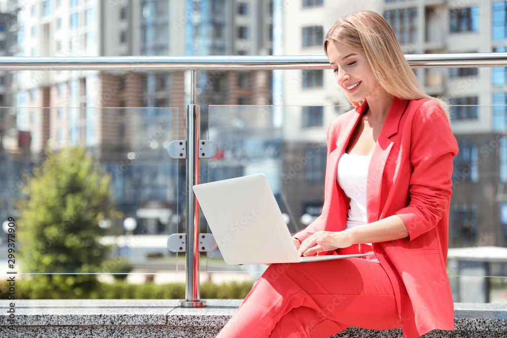 Fototapeta premium Beautiful businesswoman with laptop on city street. Space for text