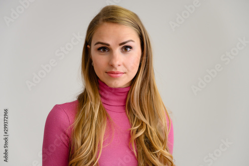 Close-up portrait of a pretty blonde girl with long curly hair standing in the studio on a white background with emotions in different poses in a pink sweater. Beauty  Model  Cosmetics