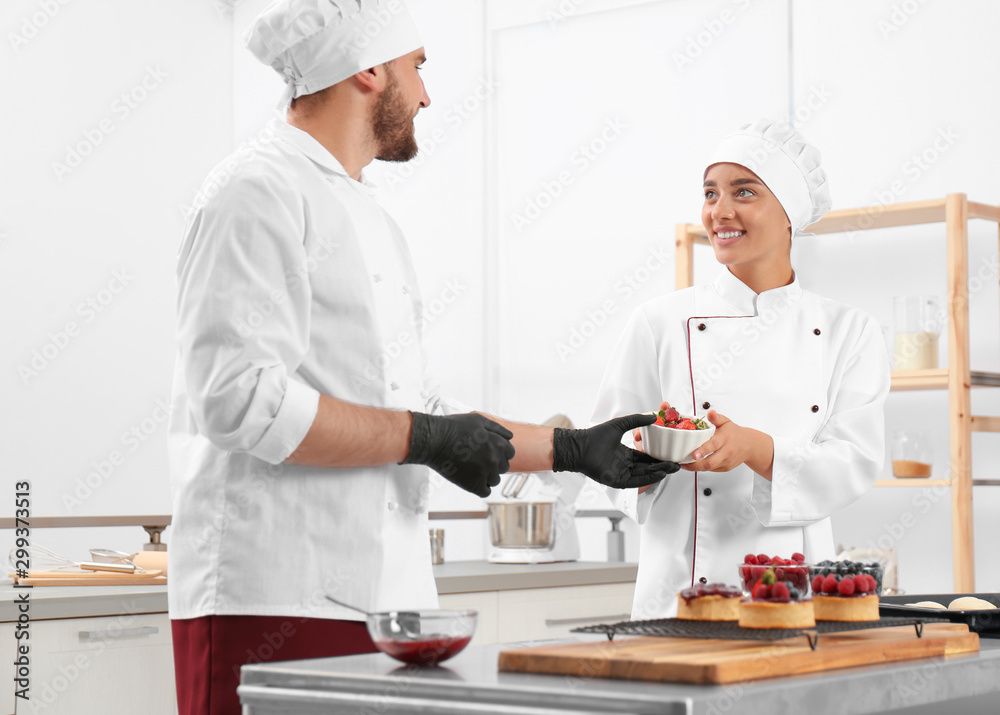 Pastry chefs preparing desserts at table in kitchen