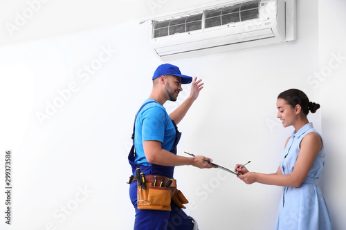 Canvas Print Professional technician speaking with woman about air conditioner indoors
