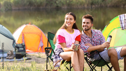 Young couple with hot drinks resting outdoors. Camping vacation