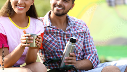 Young couple with hot drinks resting outdoors, closeup. Camping vacation