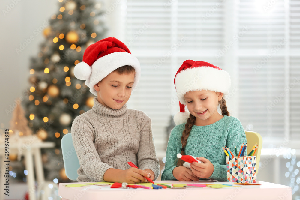 Little children in Santa hats making craftworks at table indoors. Christmas season Little children in Santa hats making craftworks at table indoors. Christmas season