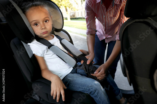 Mother fastening her daughter with car safety seat belt. Family vacation
