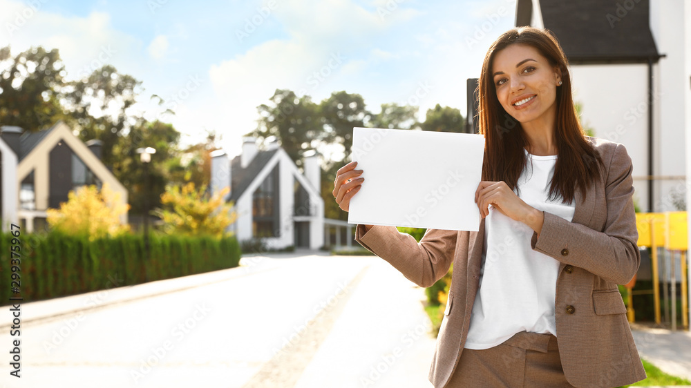 Beautiful agent holding real estate sign outdoors Beautiful agent holding real estate sign outdoors