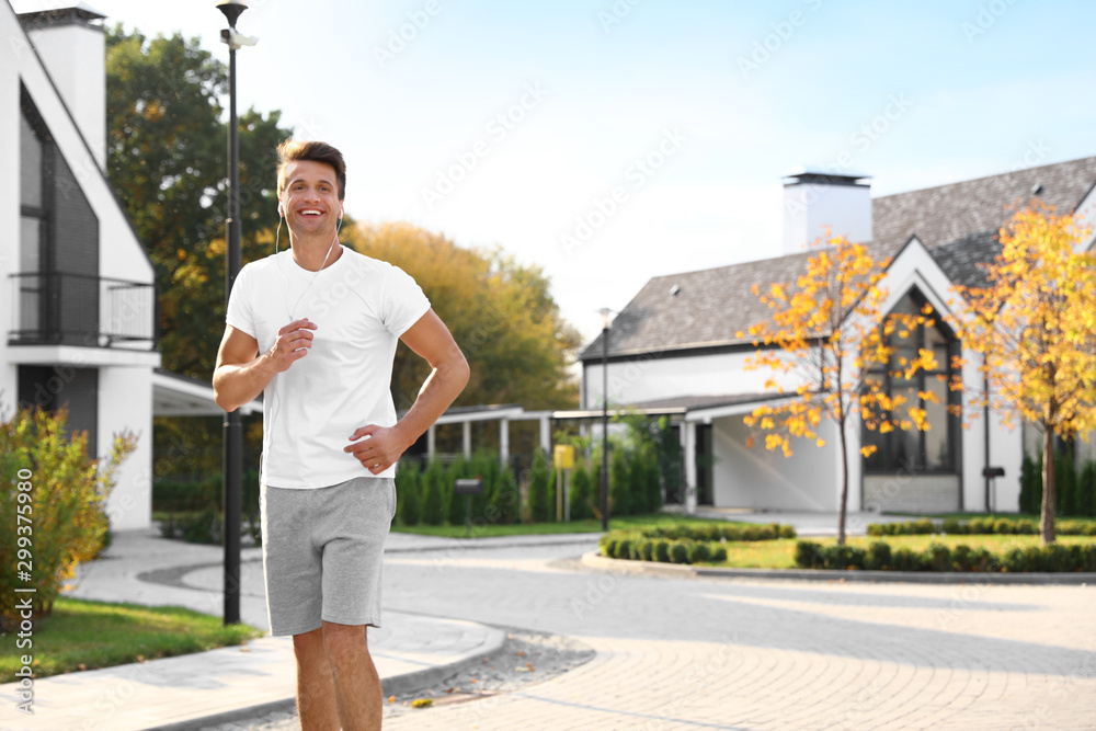 Young man with earphones running outdoors on sunny morning. Healthy lifestyle