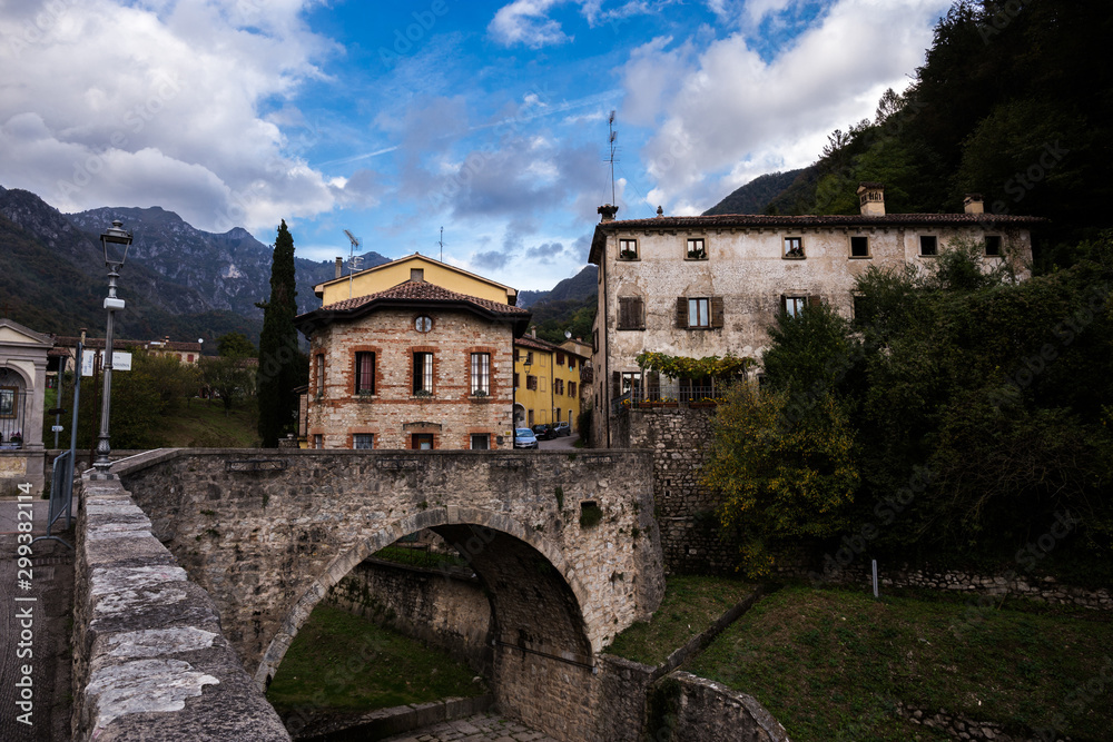 Old rural buildings with many windows,  stone bridge and beautiful blue sky with mountains in the background