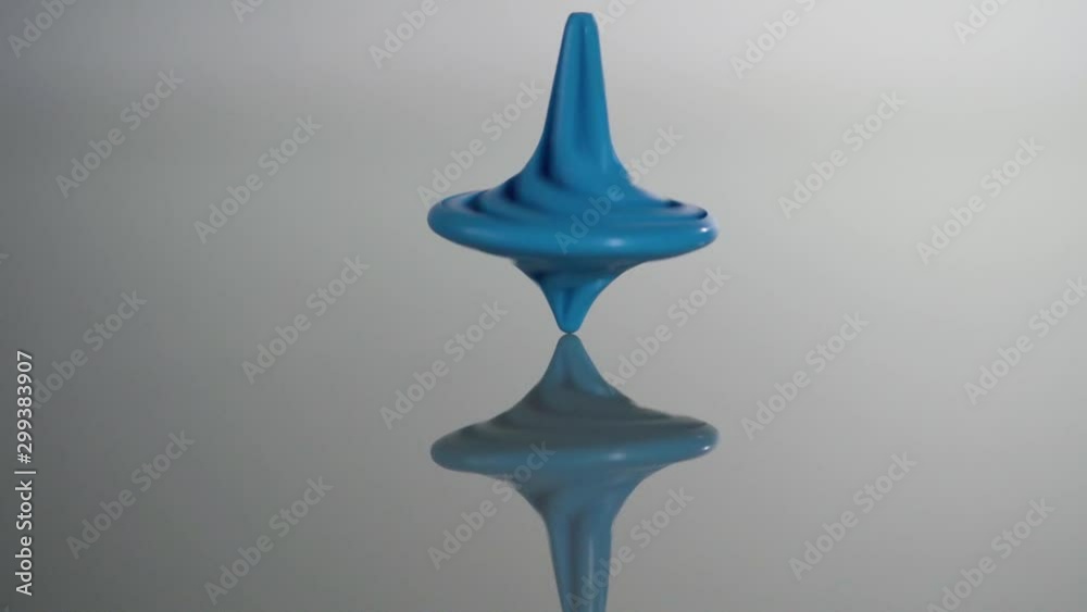 Blue spinning top spinning, wobbling and stopping. Whirligig in action is reflected on mirror surface Blue spinning top spinning, wobbling and stopping. Whirligig in action is reflected on mirror surface