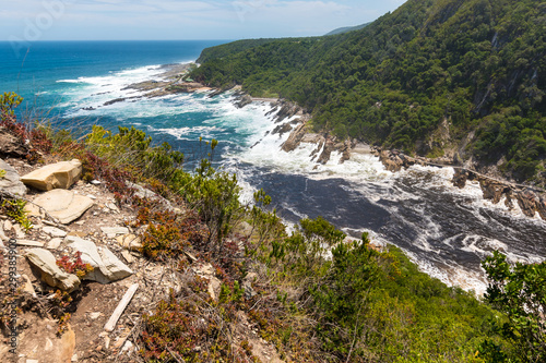 A wide view looking down on Storms River Mouth where the river meets the sea, and the suspension bridge across the river. Tsitsikamma National park, South Africa
