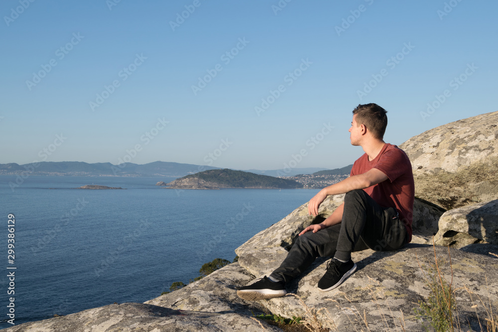 Boy sitting on the rocks of a mountain looking at the ocean