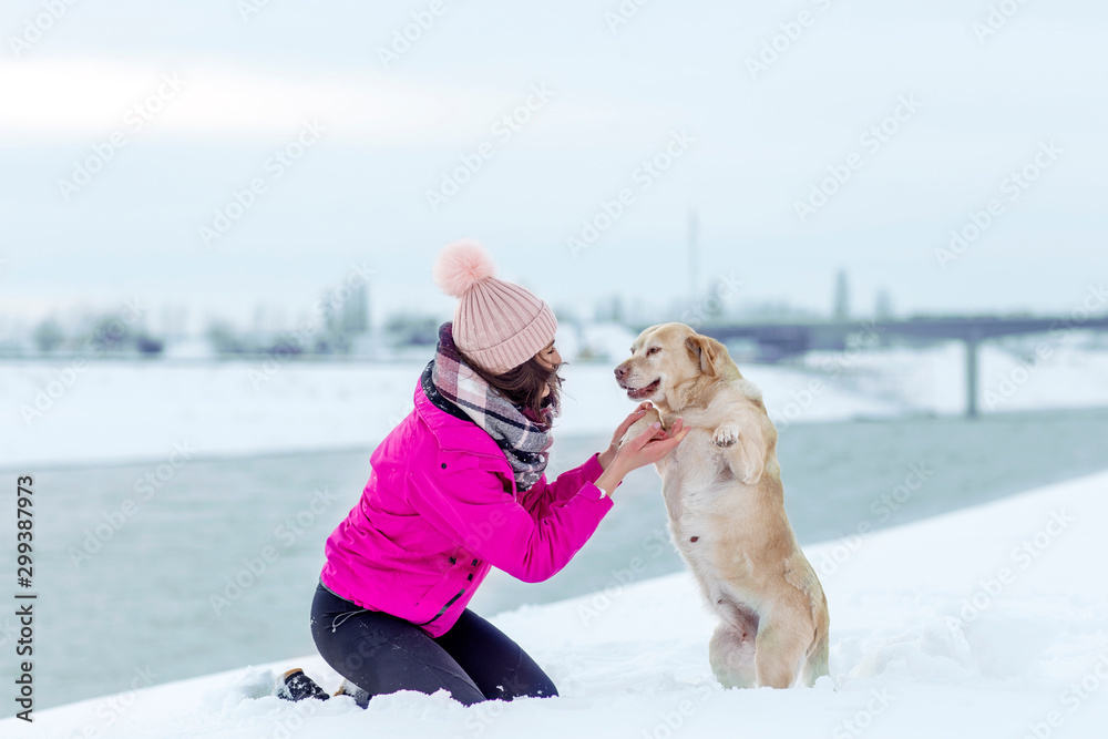 Young woman playing with her labrador ritriever in the snow on winter day
