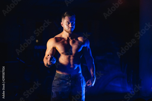 Attractive body builder posing and showing off muscles on dark black and blue background. Filters used. Naked torso. Fitness concept. Closeup.