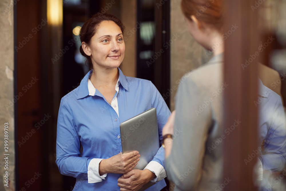 Mature businesswoman holding laptop computer and talking to the employee at the office