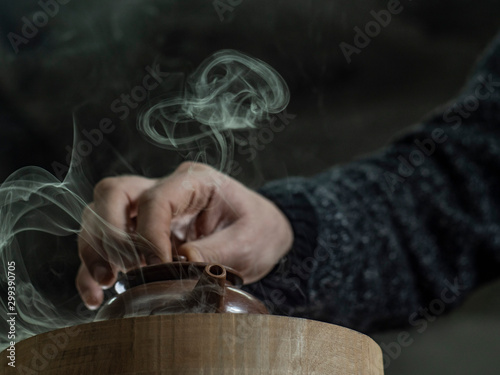 close-up male hand closed the lid of a clay teapot made of yixing clay. beautiful steam from a clay teapot. Yixing clay teapot. brown pottery teapot