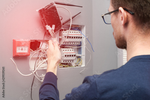Fotografie A man with glasses opposite the circuit breakers with wires and a router