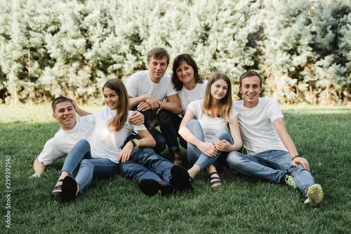 Happy family in white T-shirt and jeans sitting on the green grass. Parents with their adult children walking in the park. Family time concept