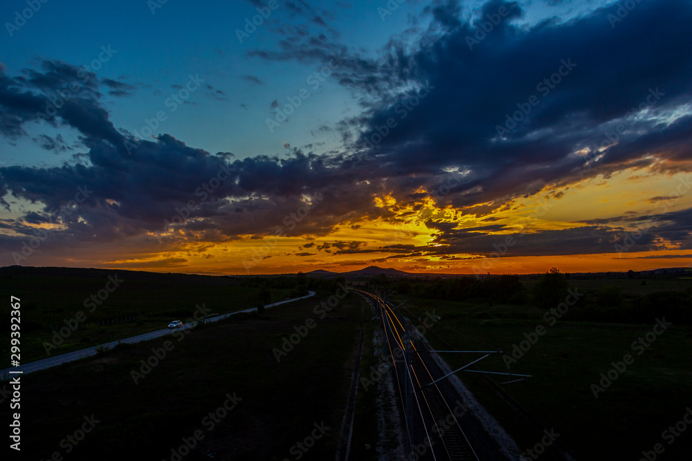 Scenic sunset over sunlit empty railway tracks and asphalt road near Krum, Southern Bulgaria, elevated view from a bridge