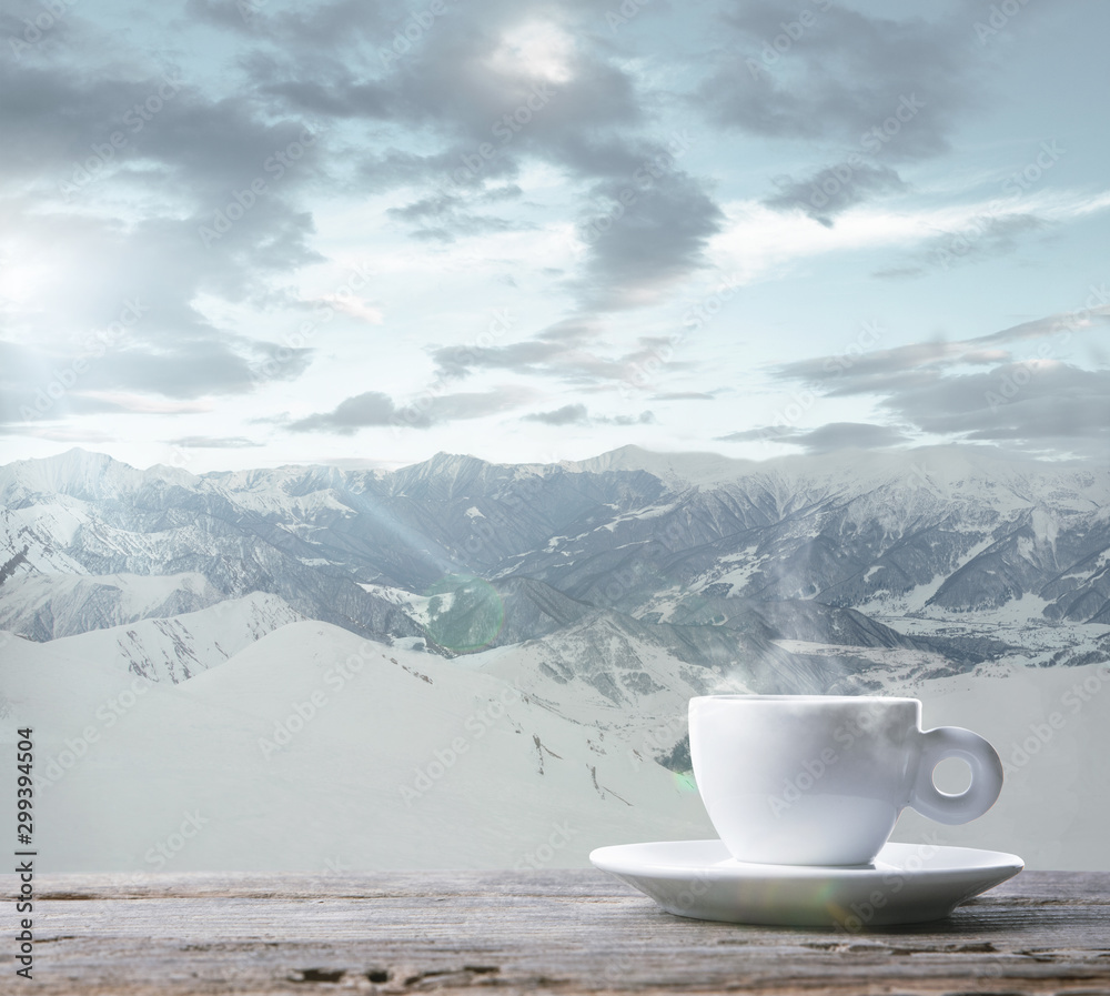 Single tea or coffee cup and landscape of mountains on background. Cup of hot drink with snowly look and cloudly sky in front of it. Warm in winter day, holidays, travel, New Year and Christmas time.