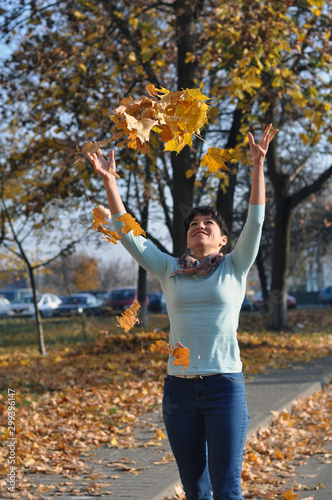 season and people concept - happy young woman throwing maple leaves and having fun in park