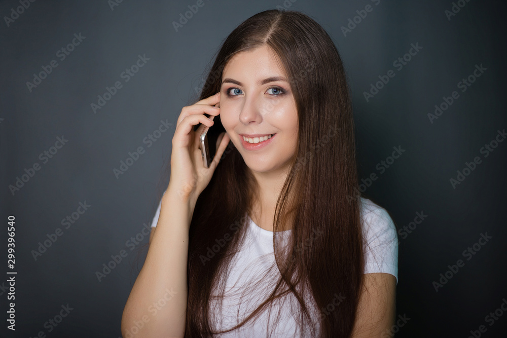 young, beautiful girl in a white T-shirt and blue jeans with a smartphone in her hands. Studio photo on a gray background. young, beautiful girl in a white T-shirt and blue jeans with a smartphone in her hands. Studio photo on a gray background.