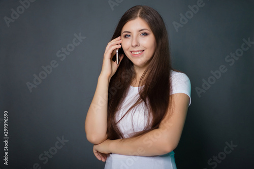 young, beautiful girl in a white T-shirt and blue jeans with a smartphone in her hands. Studio photo on a gray background.