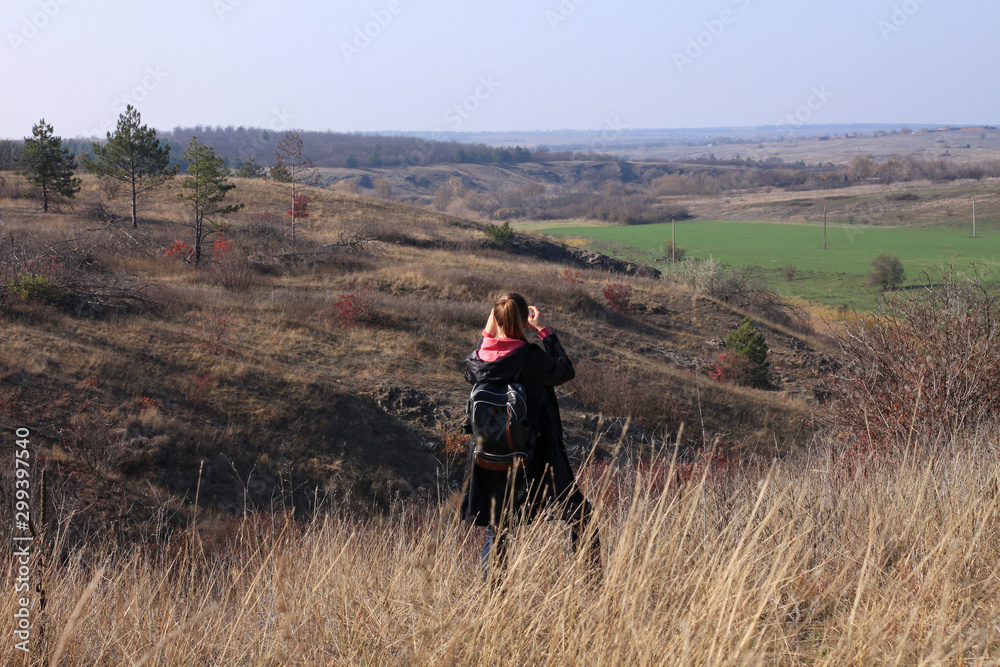 A young woman stays on a hill above the wild river and photographs the landscape. Solo travelling.