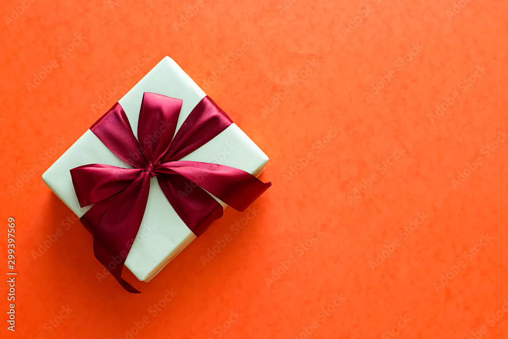 white gift box with red bow on orange background