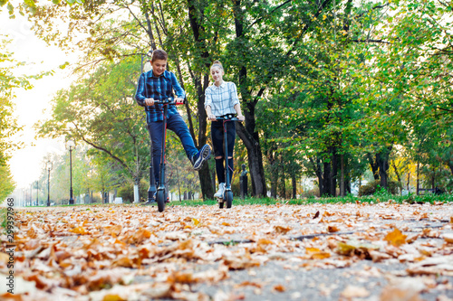 Cute teenager girl and boy riding electric kick scooter in the park.