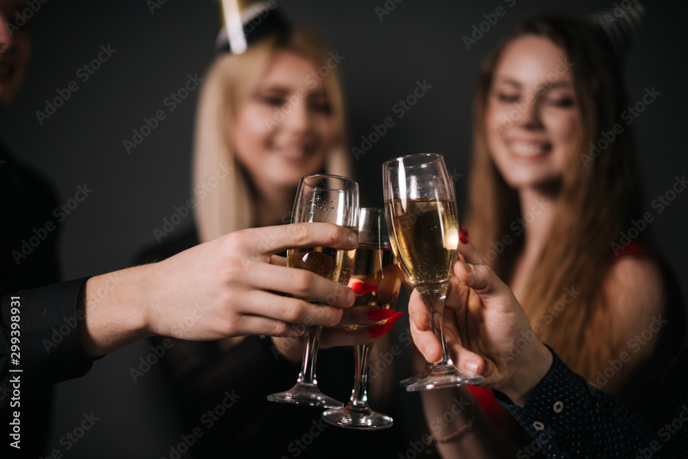 Close-up of man and woman clinking with champagne glasses. Four beautiful and cheerful friends in festive clothes on background.